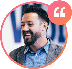 A bearded man in a gray blazer and blue checkered shirt is smiling and looking to the side, likely pondering careers. A pink and orange speech bubble with quote marks is in the top right corner. The background is blurred.