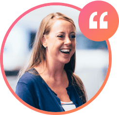 A smiling woman with long hair in a dark blue cardigan and white shirt stands against a blurred indoor backdrop. In the top right corner, a stylized orange and pink quotation mark symbol subtly hints at inspirational careers.